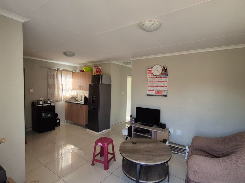 Open-plan living area featuring tiled flooring and a compact kitchen with built-in cabinetry and sink.