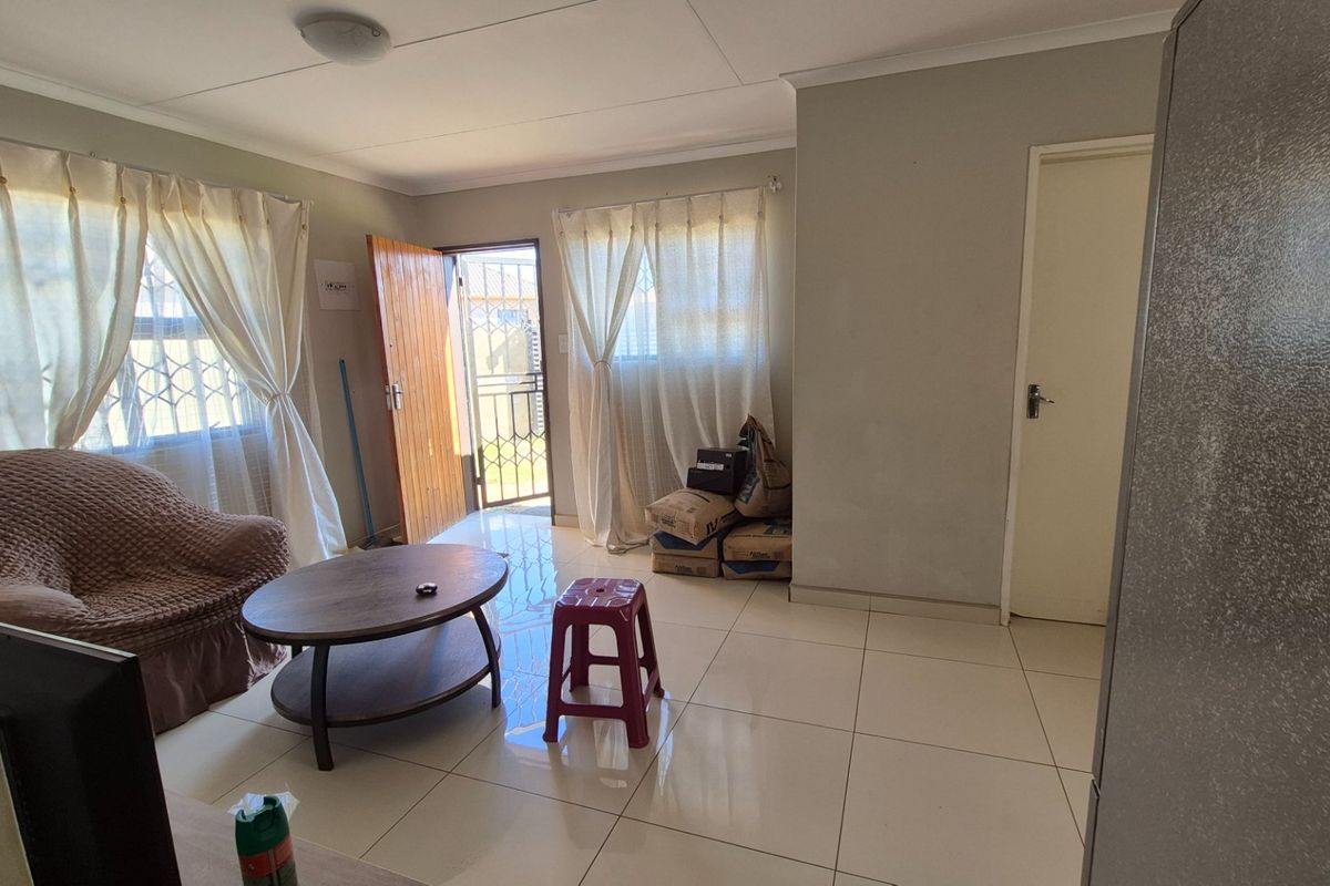 A living room featuring tiled flooring, neutral wall finishes, and direct access to the exterior via a security gate.