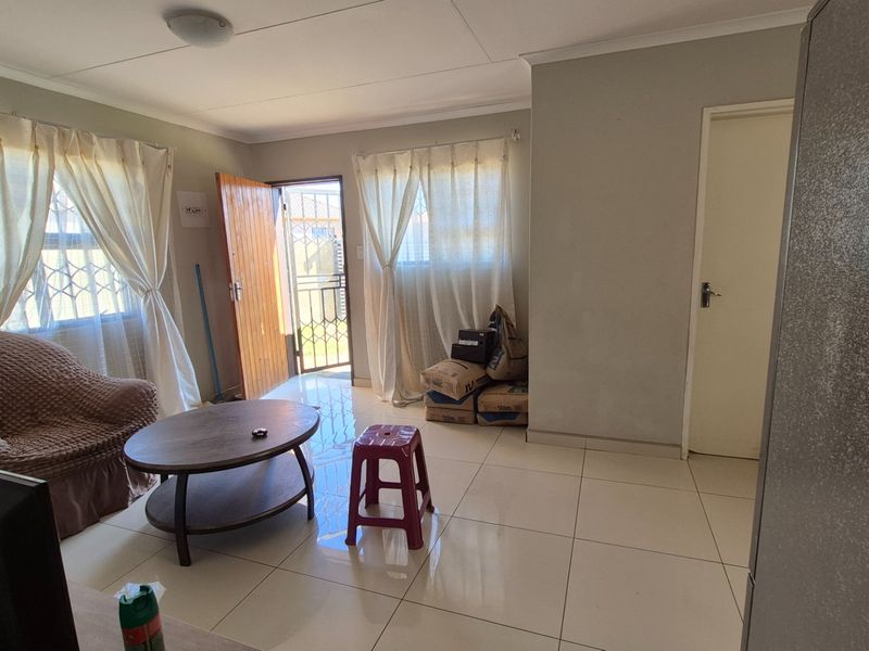 A living room featuring tiled flooring, neutral wall finishes, and direct access to the exterior via a security gate.