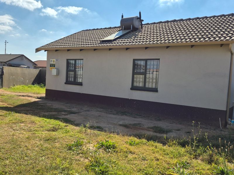 Rear view of a single-story house featuring a tiled roof with a solar water heater, security bars on windows, and a fenced yard.