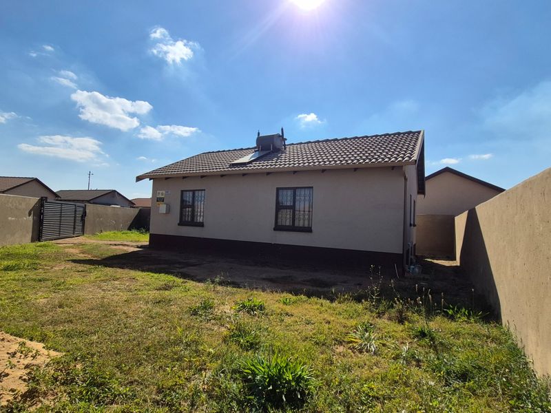 Rear view of a detached house featuring a tiled roof with a solar geyser, security bars on windows, and a large enclosed yard.