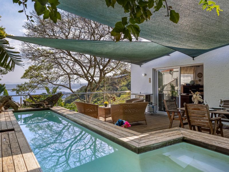 Outdoor pool area featuring timber decking, a shade sail, and a stainless steel balustrade overlooking a scenic landscape.
