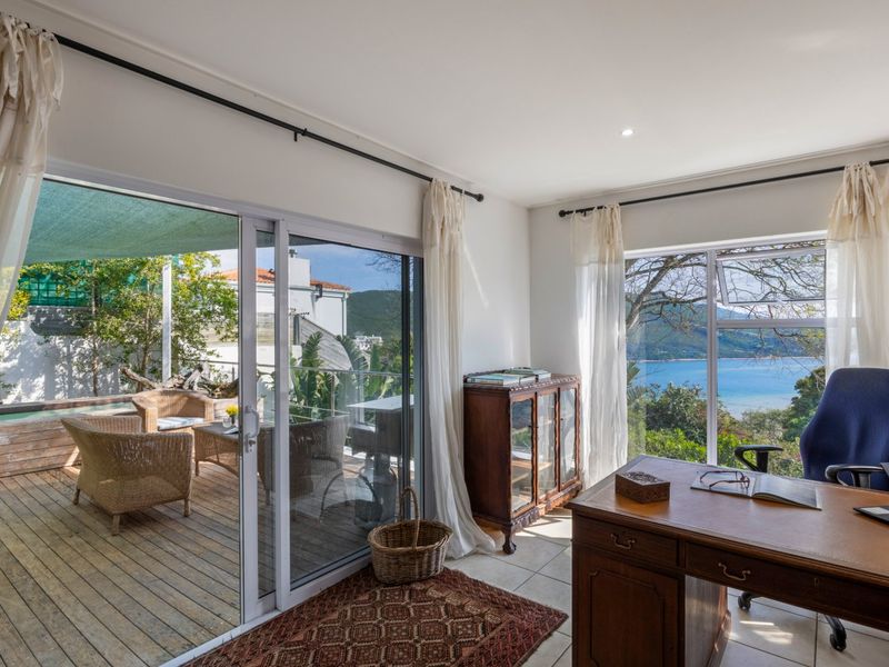 A bright home office featuring large windows and sliding glass doors that open onto a wooden deck with scenic coastal views.