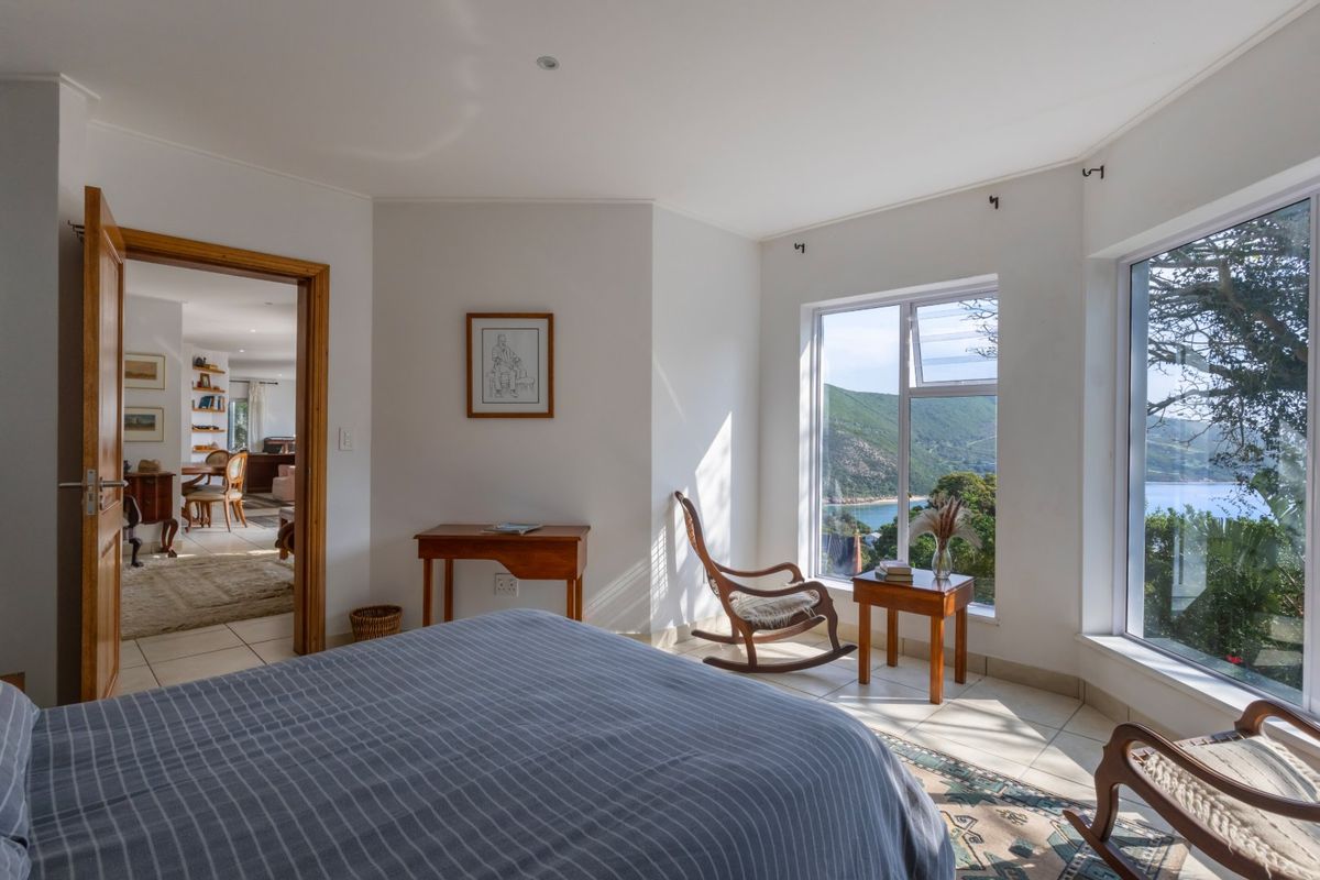 A bright bedroom featuring tiled flooring, recessed lighting, and large windows offering scenic views, with an adjoining room visible through the doorway.