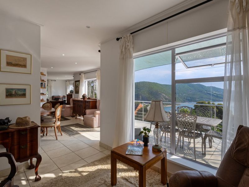 Spacious open-plan living area featuring tiled floors, recessed lighting, and large glass doors opening onto a balcony with scenic mountain and water views.