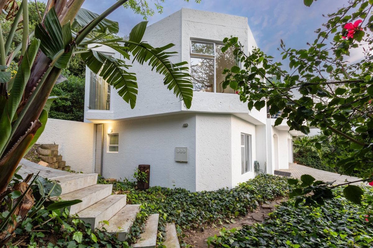 A view of the rear exterior facade featuring a modern white textured finish, concrete stairs, and established garden landscaping.