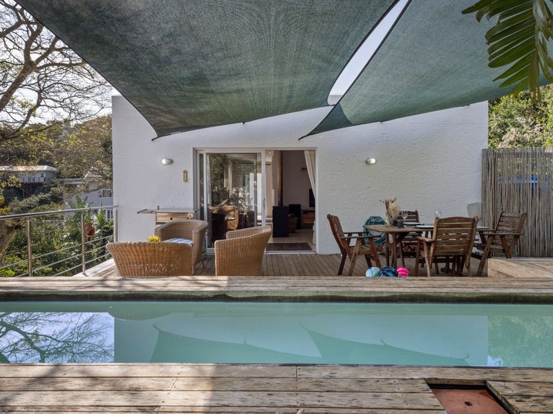 Outdoor pool area featuring timber decking, a shade sail, and direct access to the interior through sliding glass doors.