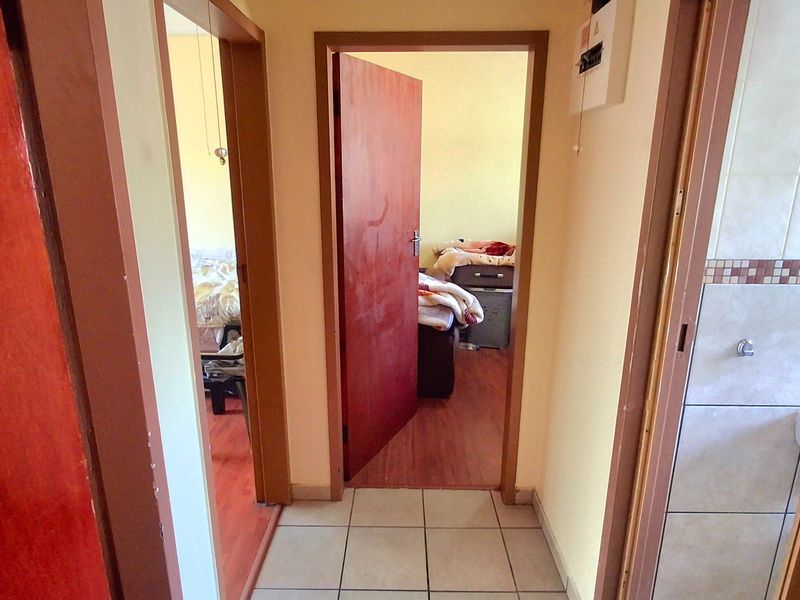 A functional hallway connecting multiple rooms, featuring tiled flooring and standard wooden door frames, providing access to the bedroom and bathroom areas.