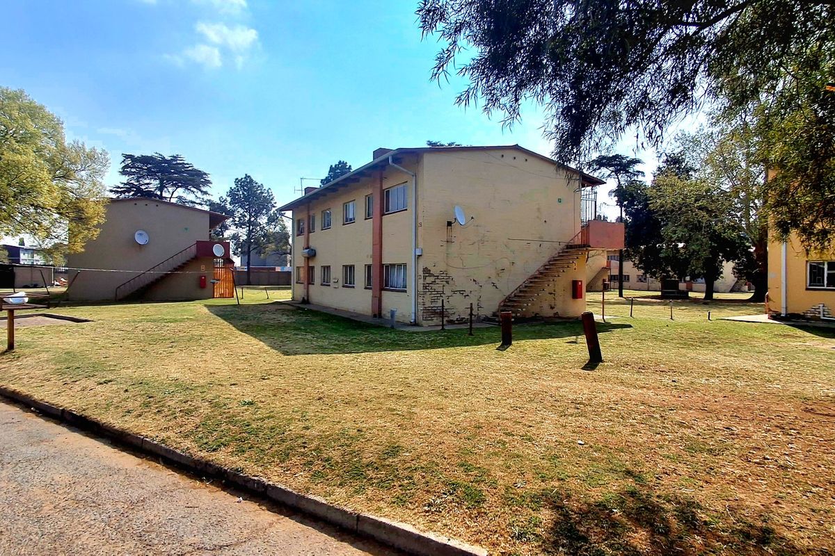 Exterior view of a multi-story apartment block featuring external staircases, satellite dishes, and surrounding communal garden space.
