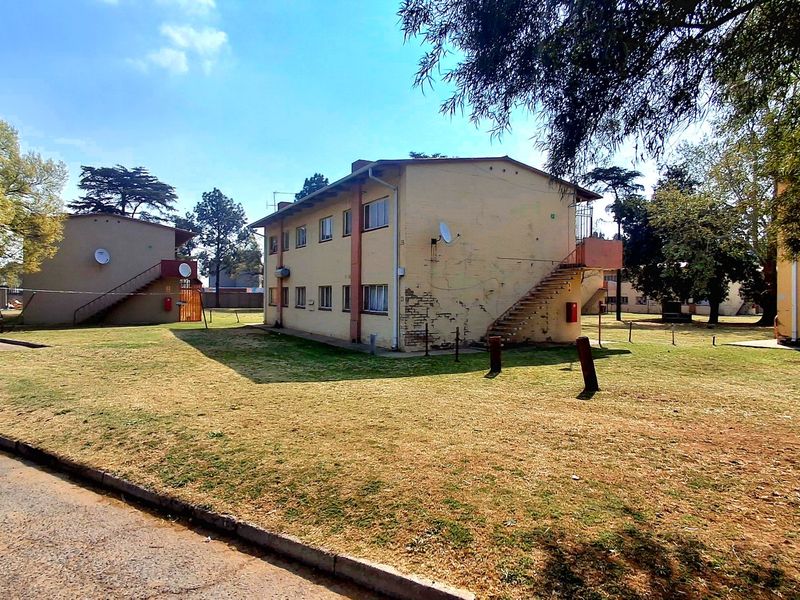 Exterior view of a multi-story apartment block featuring external staircases, satellite dishes, and surrounding communal garden space.