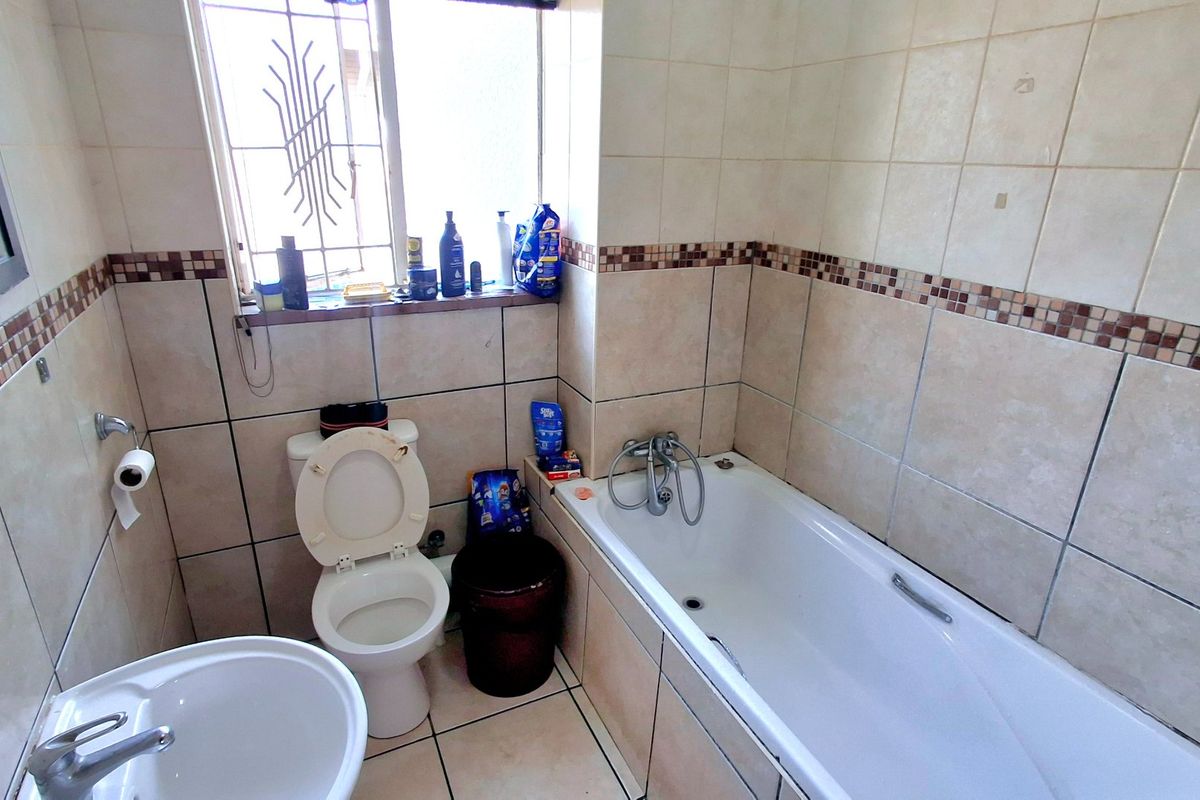 A functional bathroom featuring a bathtub, pedestal basin, and toilet with neutral wall and floor tiling.