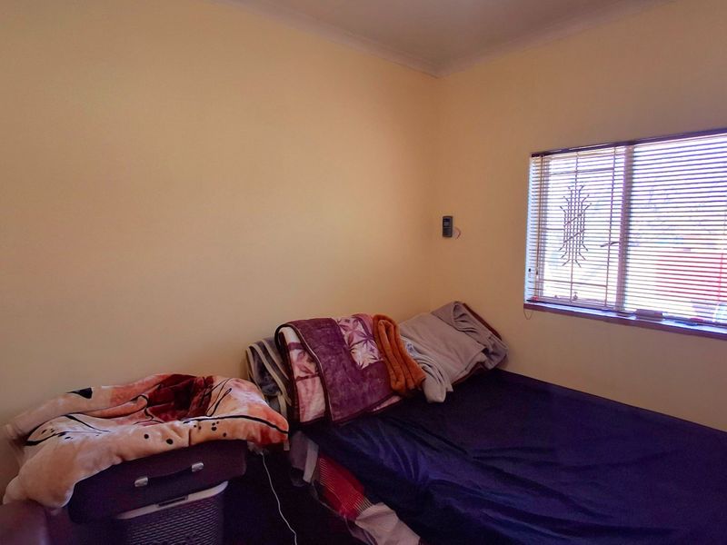 A functional bedroom featuring security bars on the window and venetian blinds, providing a basic and private living space.