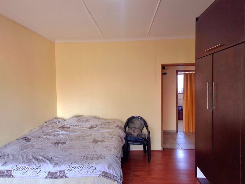 A bedroom featuring laminate flooring and a built-in wardrobe, with access to an adjacent room through a doorway.