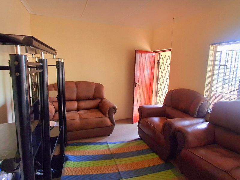 A living room featuring a security gate and window blinds, providing a functional space with neutral wall finishes.