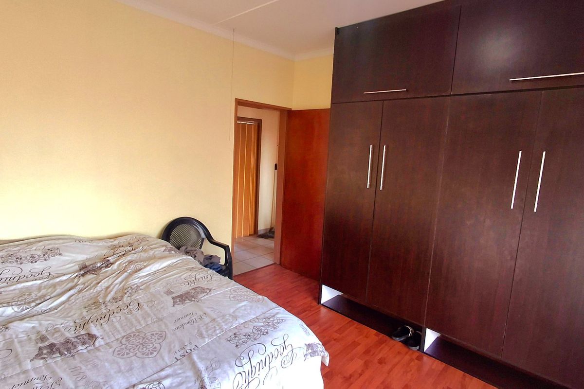 A bedroom featuring dark wood-finish built-in cupboards and laminate flooring, providing functional storage and a neutral living space.