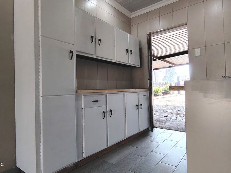 A functional scullery or utility area featuring built-in cabinetry, tiled walls, and direct access to the exterior.