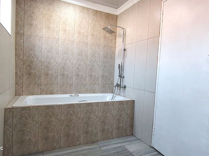 A functional bathroom featuring a built-in bathtub with a modern shower head and neutral wall tiling.