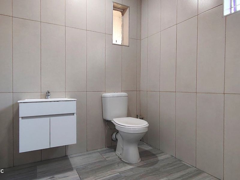 A clean, modern bathroom featuring neutral wall tiles, wood-look floor tiles, a wall-mounted vanity, and a standard toilet.