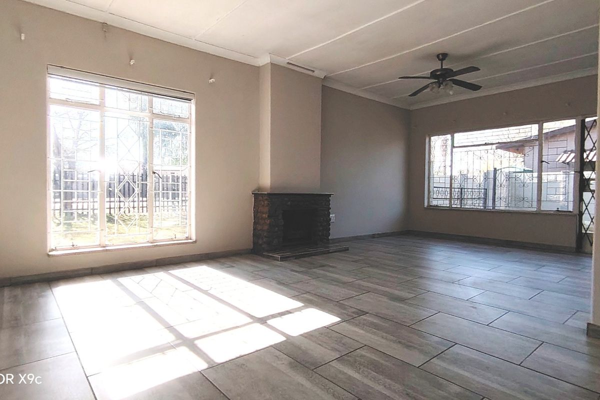 Spacious living room featuring a stone fireplace, tiled flooring, and a ceiling fan, with large windows fitted with security bars.