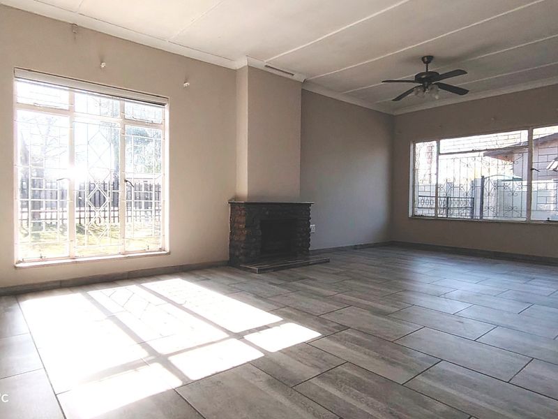 Spacious living room featuring a stone fireplace, tiled flooring, and a ceiling fan, with large windows fitted with security bars.
