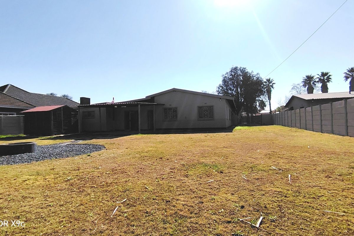 Rear view of the property featuring a large garden, precast boundary wall, and a covered patio area.