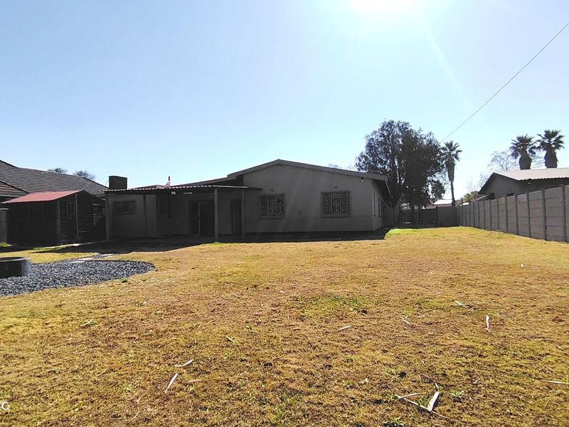 Rear view of the property featuring a large garden, precast boundary wall, and a covered patio area.