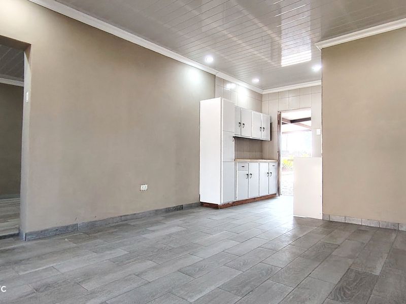 An empty kitchen area featuring tiled flooring, built-in white cabinetry, and recessed ceiling lighting, providing a clean and functional space ready for customization.