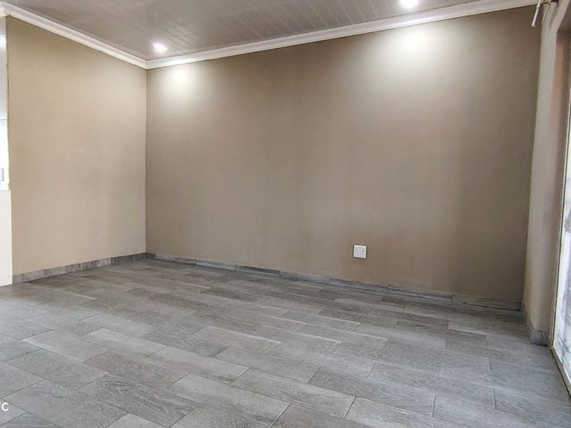 An empty open-plan living area featuring modern grey tiled flooring, neutral walls, recessed ceiling lights, and a large sliding glass door.