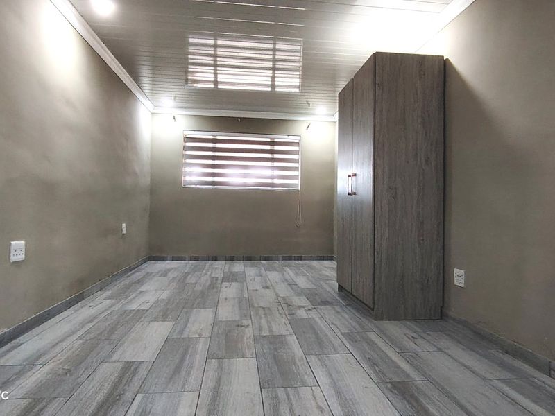 A bedroom featuring wood-look tiled flooring, recessed ceiling lighting, and a built-in wardrobe, providing a clean and functional living space.