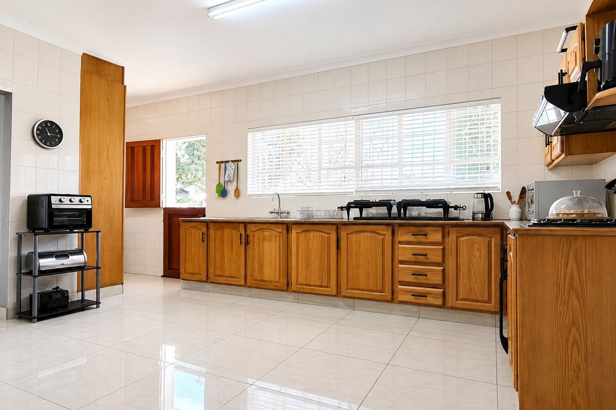 A functional kitchen featuring wooden cabinetry, tiled splashbacks, and tiled flooring, offering a clean and practical workspace with natural light.