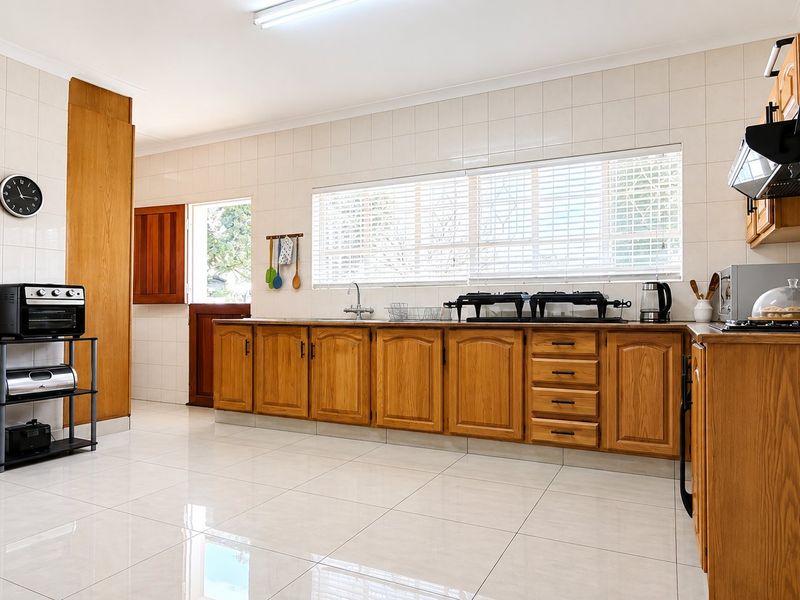 A functional kitchen featuring wooden cabinetry, tiled splashbacks, and tiled flooring, offering a clean and practical workspace with natural light.