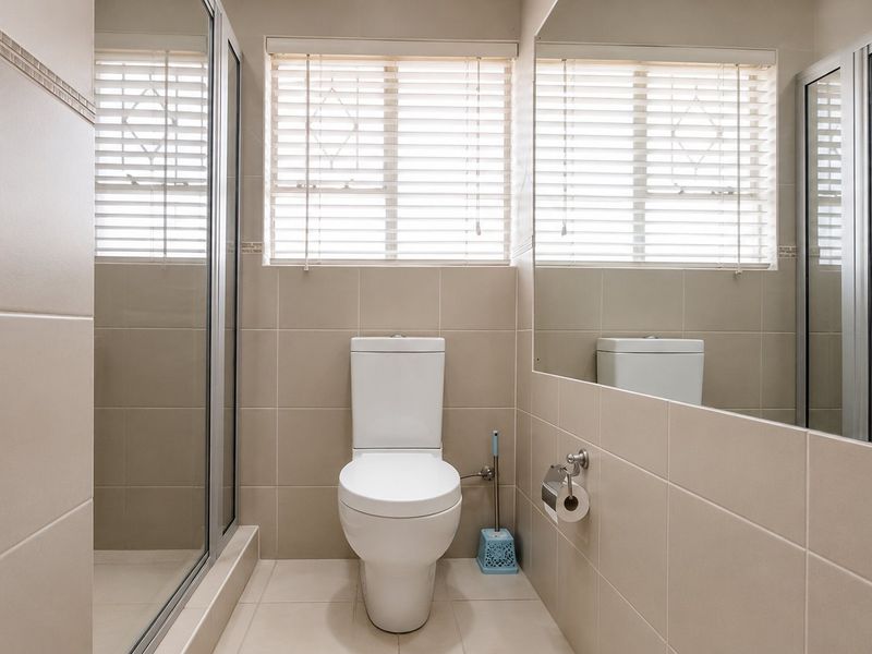 A clean, modern bathroom featuring a glass-enclosed shower, a white toilet, large wall mirror, and neutral floor-to-ceiling tiling.