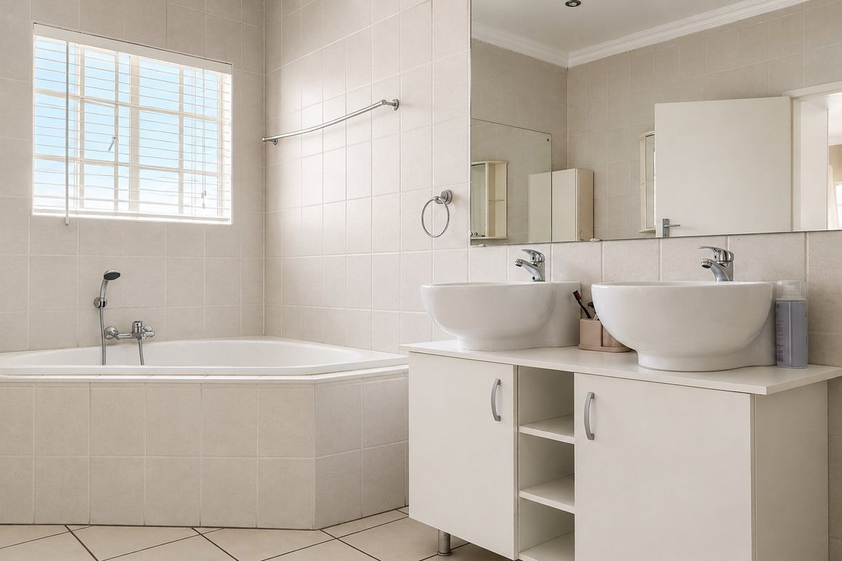 A bright, neutral-toned bathroom featuring a corner bathtub, a double vanity with vessel sinks, and large wall-mounted mirrors.