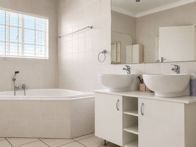 A bright, neutral-toned bathroom featuring a corner bathtub, a double vanity with vessel sinks, and large wall-mounted mirrors.