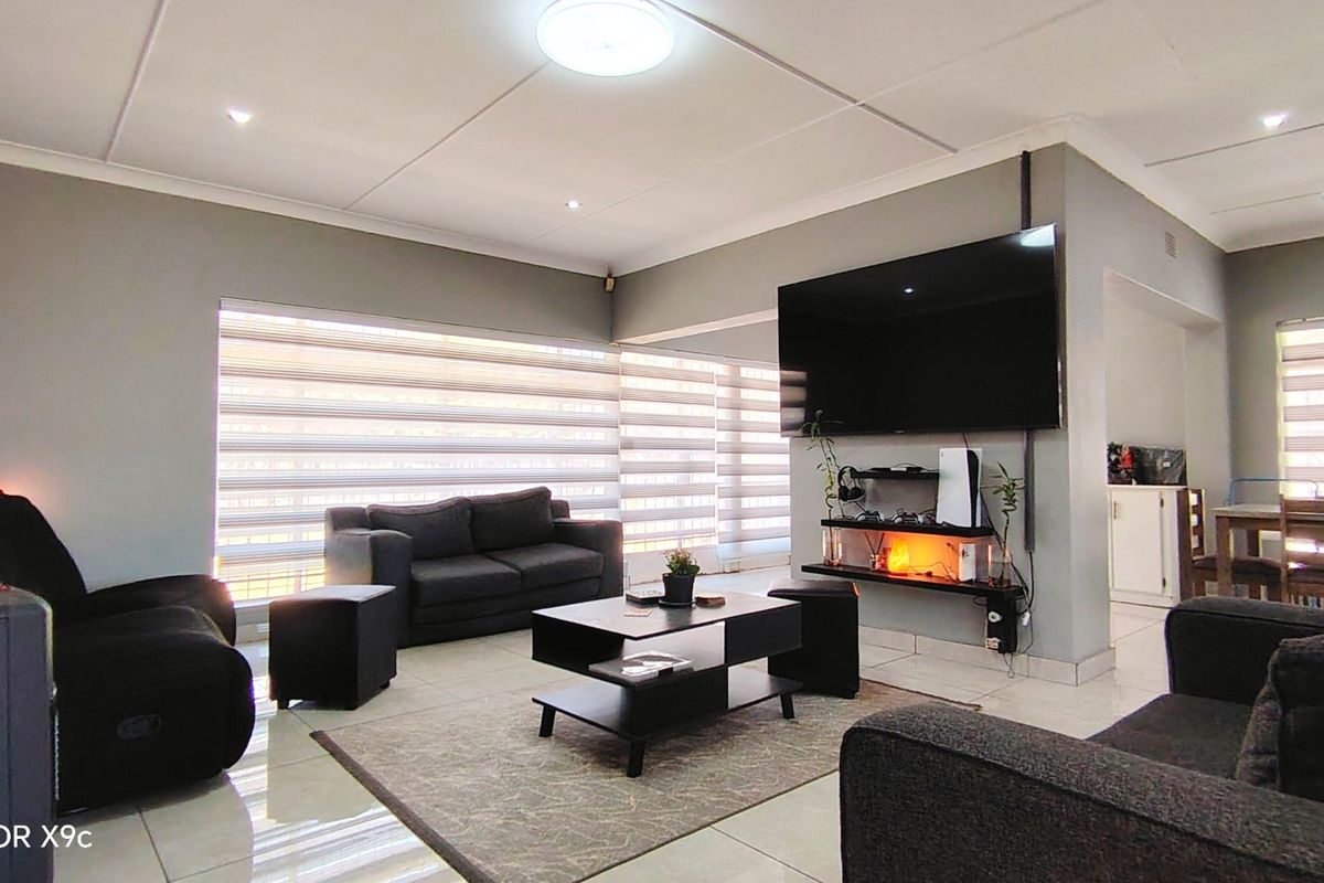 A well-maintained living room featuring tiled flooring, recessed ceiling lighting, and modern roller blinds, creating a comfortable and functional living space.