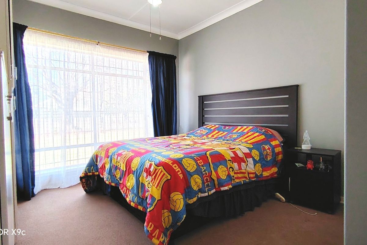 A standard bedroom featuring a large window with security bars, a ceiling fan, and neutral wall finishes.