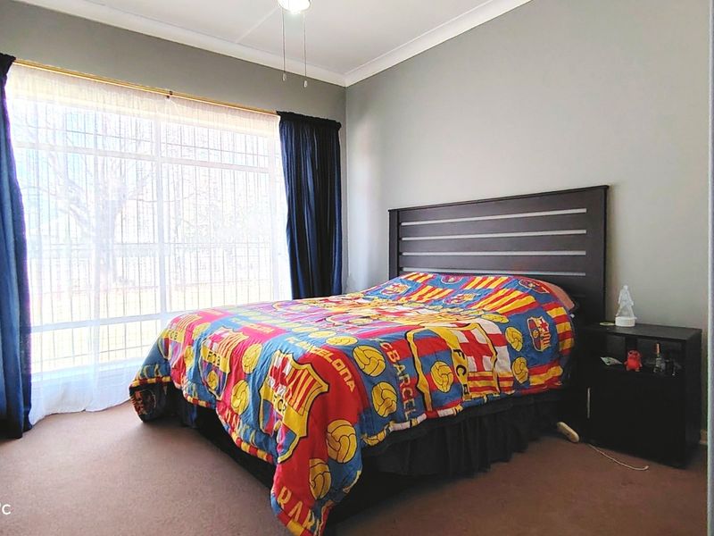 A standard bedroom featuring a large window with security bars, a ceiling fan, and neutral wall finishes.