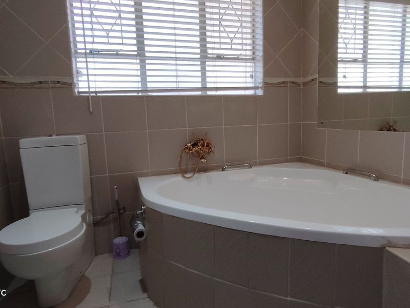 A bathroom featuring a corner bathtub, wall-mounted faucet, and toilet, finished with neutral wall tiles and venetian blinds.