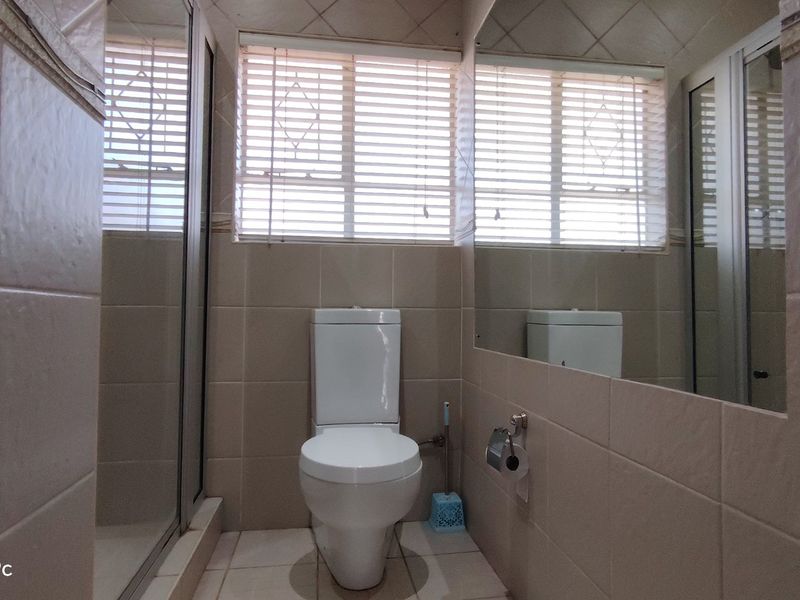 A functional bathroom featuring tiled walls and floors, a toilet, a shower enclosure, and a large wall-mounted mirror with natural light from window blinds.