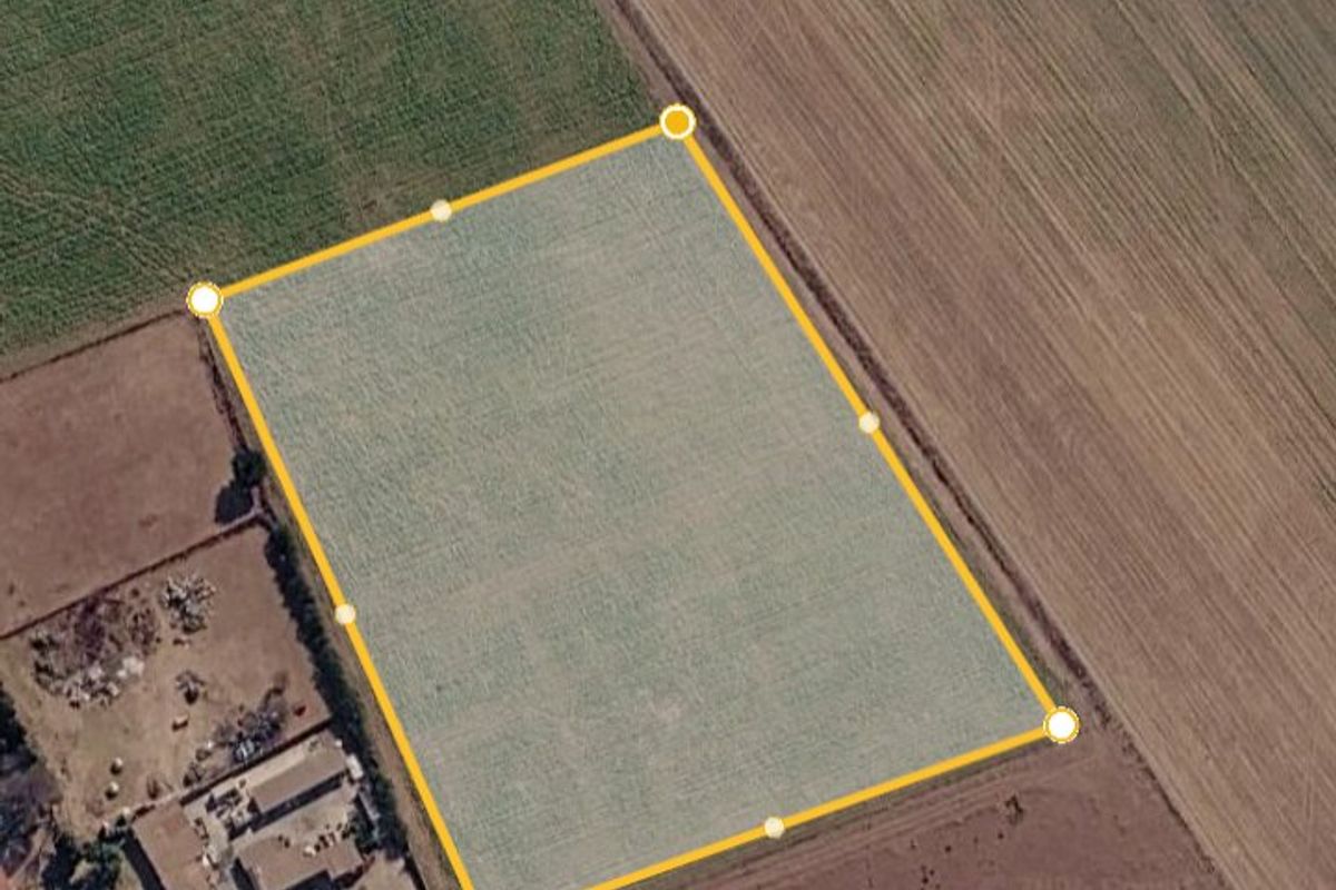 An aerial view of a vacant residential plot of land, clearly outlined with boundary markers, situated in a rural or semi-rural setting.