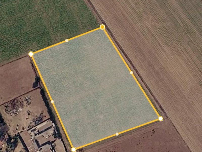 An aerial view of a vacant residential plot of land, clearly outlined with boundary markers, situated in a rural or semi-rural setting.