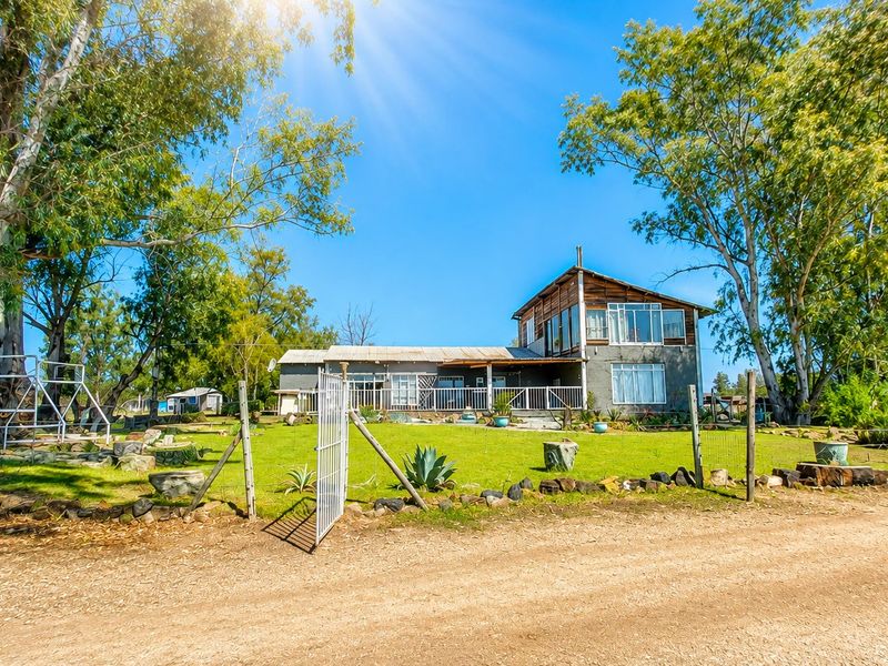 Rear view of a multi-level farm house featuring timber and masonry construction, a spacious lawn, and a metal-railed patio area.