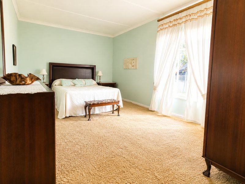 A spacious bedroom featuring neutral wall tones, carpeted flooring, and a large window with fitted curtain rods, offering a comfortable and well-maintained living space.