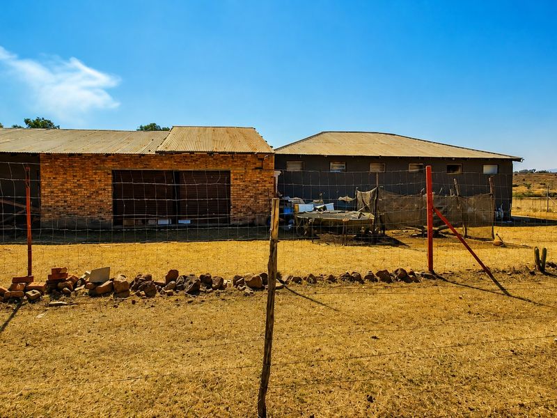 Rear view of a farm outbuilding featuring exposed brick walls, corrugated metal roofing, and metal roller doors, enclosed by wire fencing.