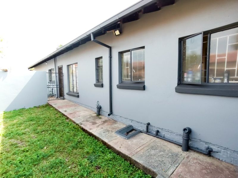 Rear exterior view of the property featuring a concrete walkway, security bars on windows, and functional drainage infrastructure.