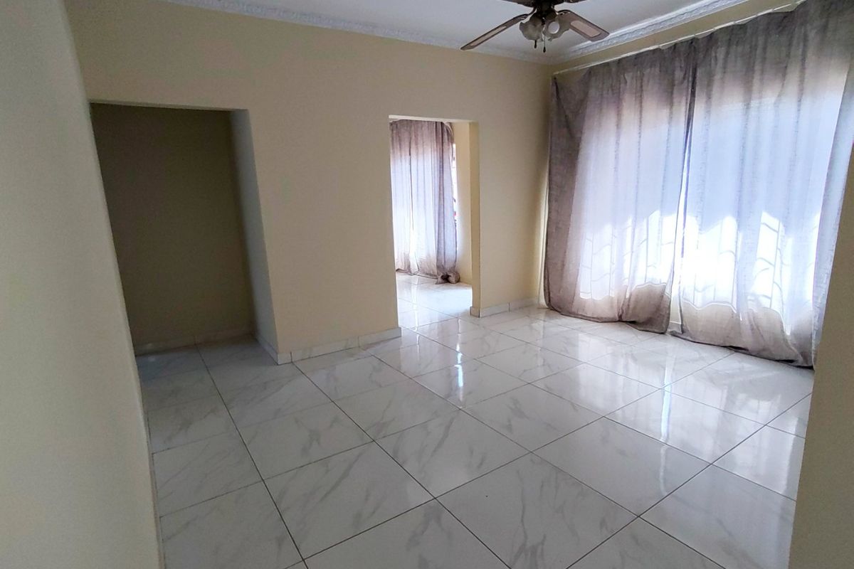 A bright, empty living room featuring modern marble-look floor tiles, a ceiling fan, and coved ceiling cornices, offering a clean and neutral space.