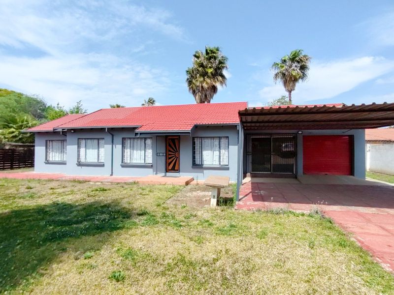 Front view of a single-story house featuring a red metal roof, attached carport, garage, and a front garden area.
