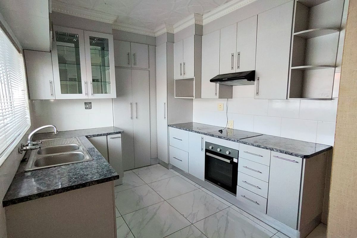 A clean, modern kitchen featuring light grey cabinetry, granite countertops, built-in oven and hob, and tiled flooring throughout.