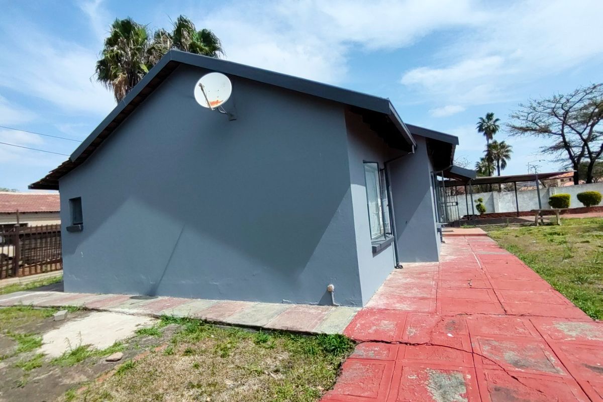 Rear exterior view of the house featuring a grey painted facade, satellite dish, and a red paved walkway leading along the side of the building.
