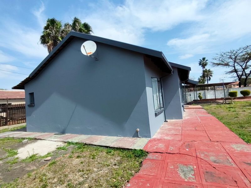 Rear exterior view of the house featuring a grey painted facade, satellite dish, and a red paved walkway leading along the side of the building.